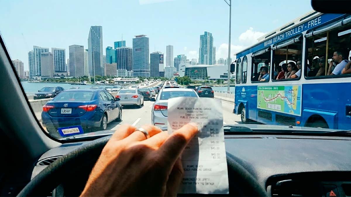 Driving across the causeway between mainland Miami and Miami Beach while holding a expensive parking garage ticket, showing the real traffic and budget impact of mixing up these two cities.